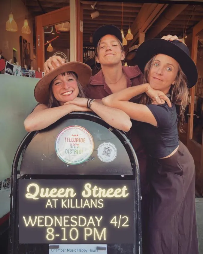 Three smiling guests posing behind the Queen Street at Killians live music event sign in Spearfish, SD